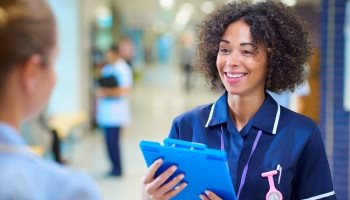 Nurse smiling and speaking to another nurse holding a clipboard.