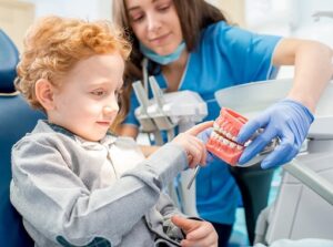 Female dentist showing the young boy artificial jaw at the dental office