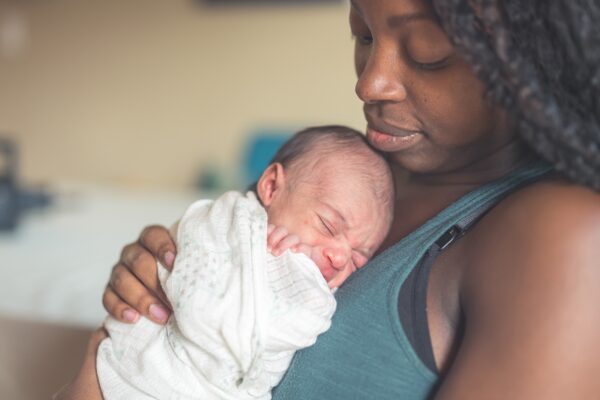 An African American mom gently cradles her newborn daughter against her chest.