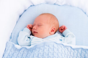 Newborn baby boy in bed. New born child sleeping under a blue knitted blanket. Children sleep. Bedding for kids. Infant napping in bed. Healthy little kid shortly after birth. Cable knit textile.