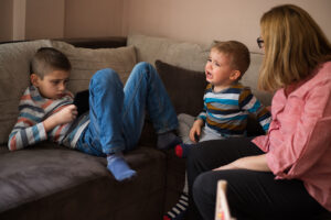 Woman looking at her sons, one is crying out loud and other one using smart phone