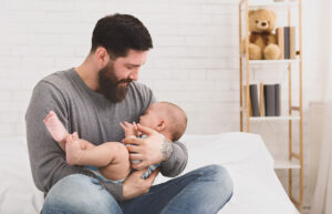 Father holding and soothing crying little newborn baby in his arms. Hungry kid looking for mothers breast
