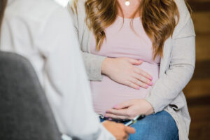 Caucasian pregnant woman is discussing something during a childbirth class or pregnancy support group. Focus on belly, no faces.