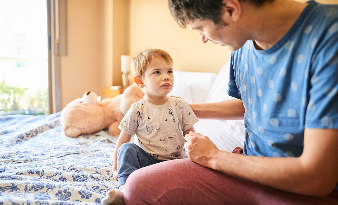 man consoling his little son sitting on bed