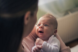 Close up of a young mother holding her two months old baby boy in her hands while standing in the bedroom