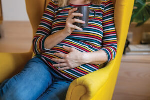 Pregnant woman holding belly while sitting in a yellow chair at living room.