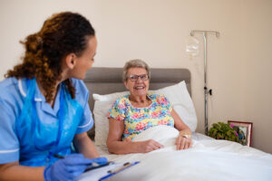 Medium view of a community nurse visiting a senior woman who is lying in her bed at home.