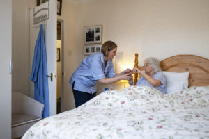 Senior woman lying in bed being helped by a home careeSenior woman lying in bed being helped by a home career