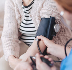 Close up view on a female nurse sitting in front of a senior patient while measuring her blood pressure during a regular visit.