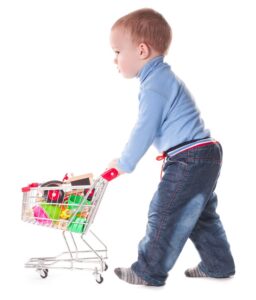 Boy plays with shopping trolley and toys, isolated on white